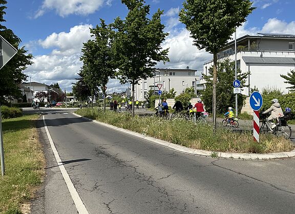 mehrere Radfahrende von hinten auf einer Straße, die in einen Kreisel führt