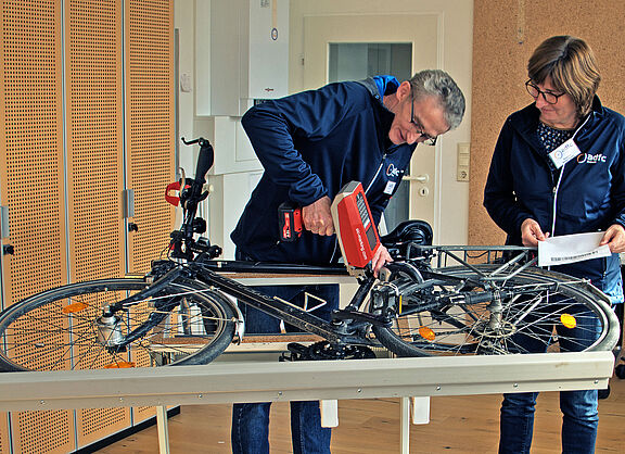 Ein Mann codiert mit einem Nadeldrucker ein auf der Seite liegendes Fahrrad, während die Besitzerin zuschaut. 